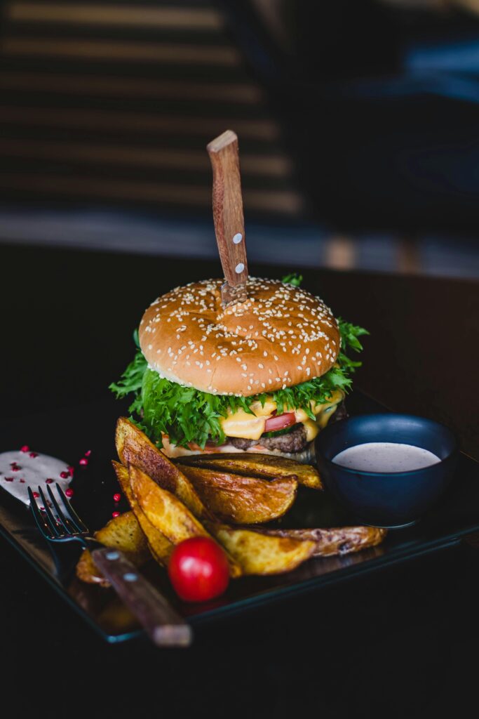 Close-up of a gourmet cheeseburger with wedges and tomato on a black plate.