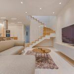 Spacious modern living room featuring stairs, a TV, and sleek furniture design.